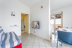 A room with a bed, a TV mounted on the wall, a dining table with chairs, and a door leading to another room.