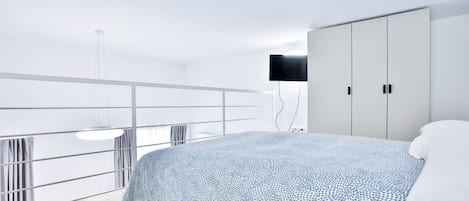 Un dormitorio moderno con una cama grande, un televisor montado en la pared y un balcón con barandilla.