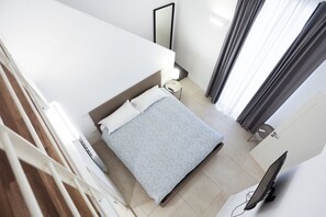 Ein Schlafzimmer mit Bett, Nachttisch, Lampe, Fernseher und einem Fenster mit Vorhängen.