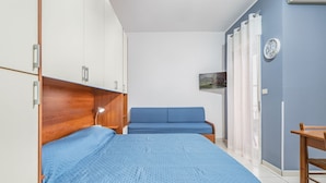 A bedroom with a bed, a blue sofa, a wooden wardrobe, and a small table. - GuestHost - Cozy Studio x2 - w/ Balcony (Chianchitta)