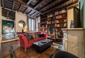 Un salon avec un canapé rouge, une table basse, une bibliothèque et une cheminée.
