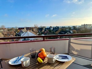 Ein Balkon mit einem für das Frühstück gedeckten Tisch, mit Blick auf ein Wohngebiet mit Häusern und blauem Himmel.
