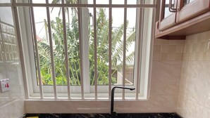 A kitchen with wooden cabinets, a black countertop, and a window with a view of greenery. - LuckySmallie 1-Bed Apartment in Goba,Dar es Salaam (Dar es Salaam)