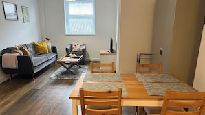 Una sala de estar con sofá, una mesa de centro, una mesa de comedor con sillas, un televisor y una ventana con persianas.