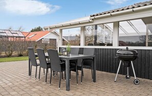 Eine Terrassensitzgelegenheit mit Tisch und Stühlen, einem Grill und Blick auf ein Haus mit rotem Dach.