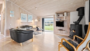 Ein gemütliches Wohnzimmer mit einer schwarzen Ledersofa, einem Holzstuhl, einem Fernseher und einem Kaminofen.
