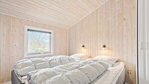 Ein Schlafzimmer mit Holzwänden, einem Fenster, zwei Nachttischlampen und einem Bett mit weißer Bettwäsche.