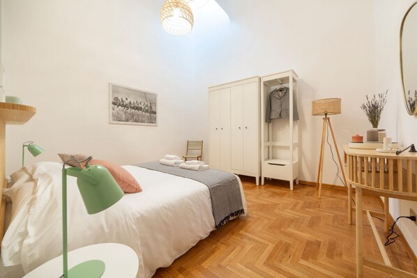 Een slaapkamer met een bed, een bureau, een kledingkast, een lamp en een spiegel.