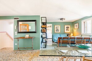 Een woonkamer met een glazen tafel, een blauwe bank en een boekenkast.