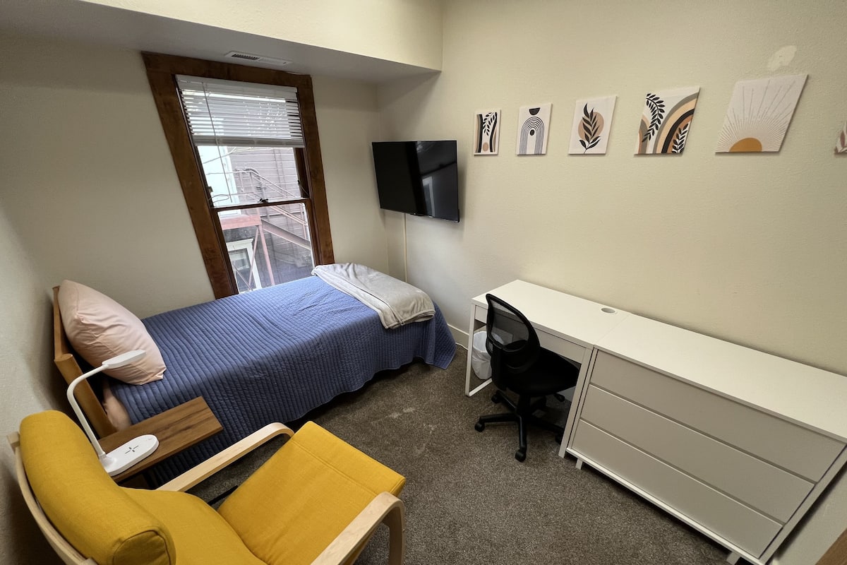 Un dormitorio con cama, escritorio, silla y televisor.