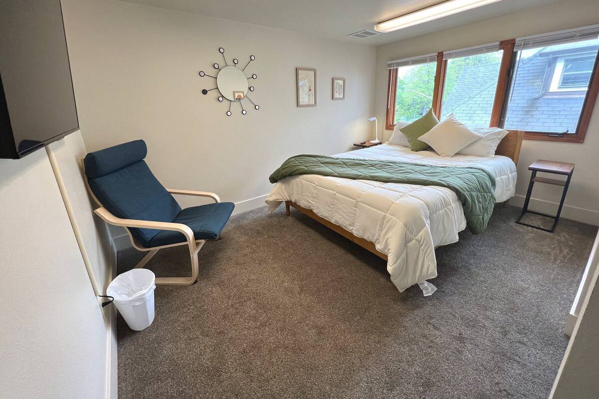 Un dormitorio con cama, una silla, una mesita y un ventanal.