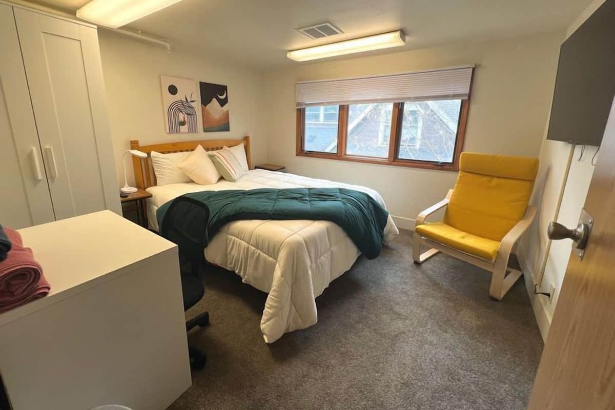 Un dormitorio con cama, una silla, un escritorio y un armario.