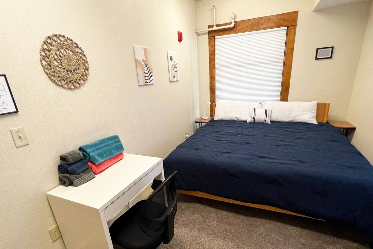 Un dormitorio con una cama, un escritorio, una silla y una ventana con persianas.