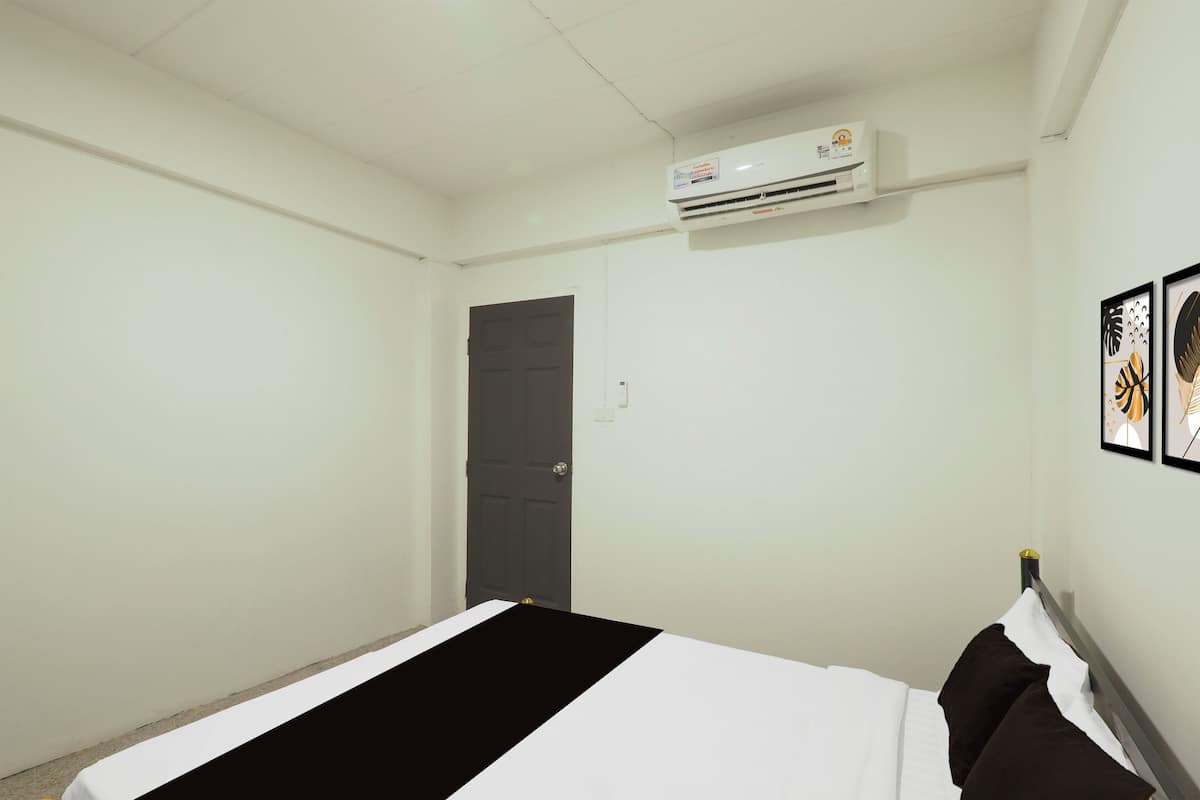 A bedroom with a bed, a door, an air conditioning unit, and framed artwork on the wall.