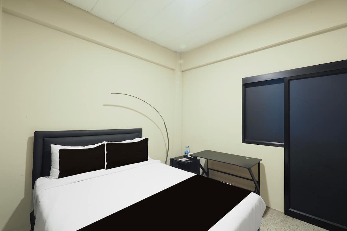 A hotel room with a bed, a desk, a water bottle, and a wardrobe.