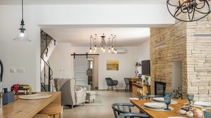 A modern kitchen with a wooden island, bar stools, and a dining area with a wooden table set for four. There is a staircase leading to another level, a stone fireplace, and a chandelier. - Nature Villa Frangipane with Pool, Drivenik, Croatia (Drivenik)