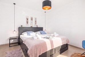 Une chambre à coucher moderne avec un lit, des tables de chevet, une commode, une lampe suspendue et des œuvres d’art murales.