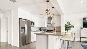 A modern kitchen with white cabinetry, stainless steel appliances, a central island, pendant lighting, and a flat-screen TV. - 6 Bedrooms, 9 Beds, 3 Bathrooms, an 82° Heated Pool, & the BEST 102° Spillover Hot Tub in all of Old Town Scottsdale! (Scottsdale)
