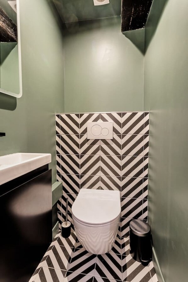 A compact bathroom with a white toilet, a sink, and a trash bin. The walls are adorned with a black and white chevron pattern.
