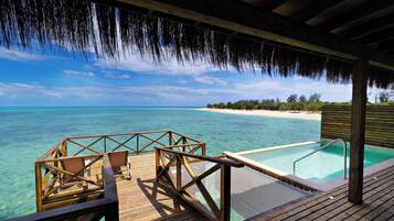 A wooden deck with chairs overlooking a clear blue sea and a pool.