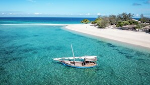 Un bote en aguas turquesas cristalinas cerca de una playa arenosa con bungalós sobre el agua.