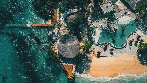 Vista aérea de un complejo turístico con playa, piscina y zona de comedor.
