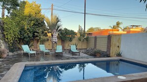 A swimming pool with four lounge chairs, surrounded by a stone patio and various plants. - Amorito Guest house, Pool, 1 block from beach, 6 blocks from downtown  (Loreto)