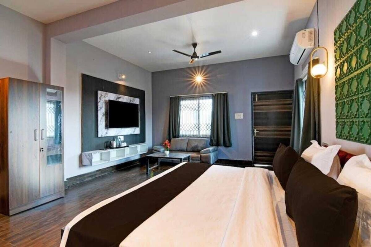 A modern hotel room with a large bed, a sofa, a TV, and a ceiling fan.
