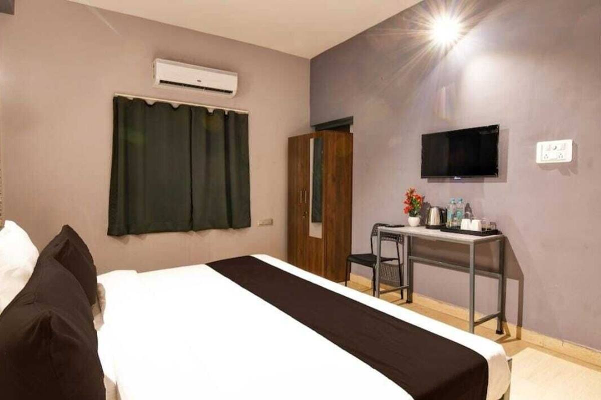 A hotel room with a bed, an air conditioning unit, a TV, a desk with a chair, and a wardrobe.