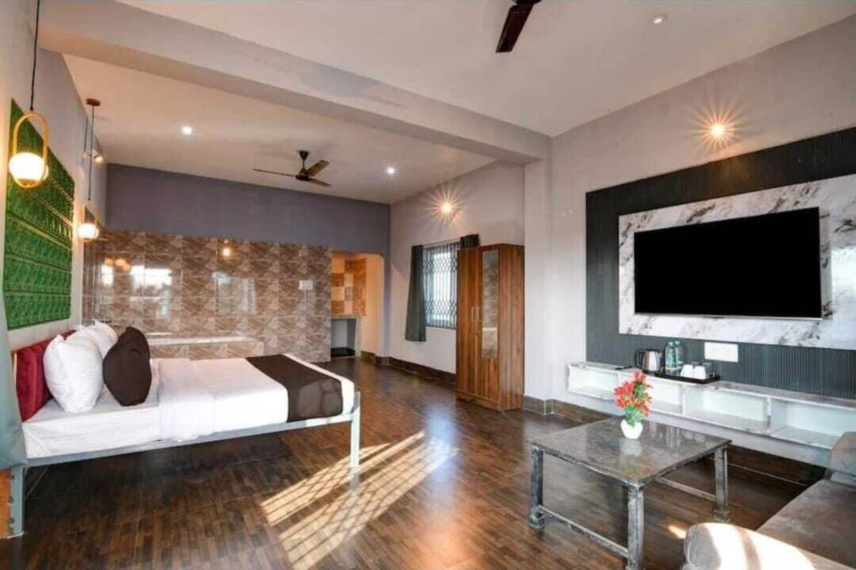 A modern living room with a sofa, a coffee table, a TV mounted on the wall, and a bed with pillows.