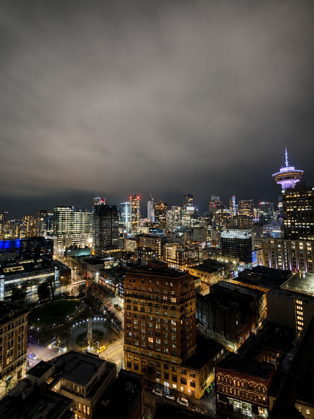 Une vue nocturne d’une ville, avec des bâtiments illuminés et une tour imposante.