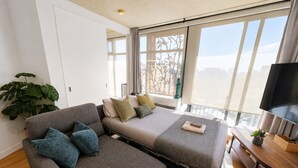Ein modernes Zimmer mit einer Couch, zwei Betten, einem Fernseher und einem großen Fenster.