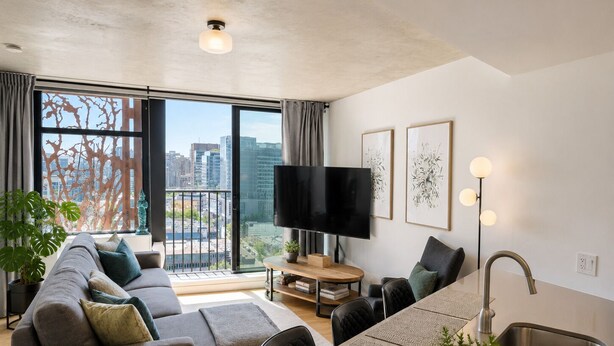 Eine moderne Wohnung mit Wohnbereich, Küchenzeile und großen Fenstern mit Blick auf die Stadt.