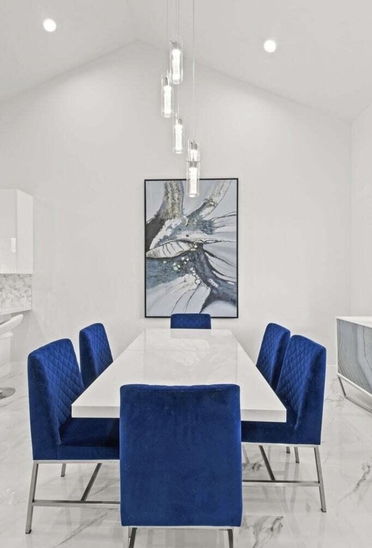 Un comedor moderno con una mesa larga, sillas tapizadas en azul y un gran cuadro abstracto en la pared.