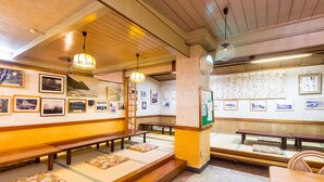 Une pièce de style japonais traditionnel, avec des tatamis, des bancs en bois et un mur orné de tableaux et de calligraphies encadrées.