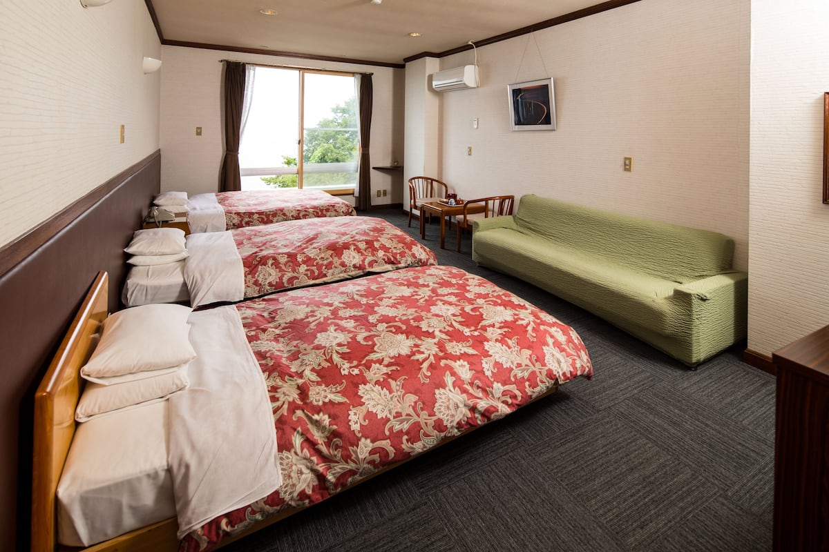 Une chambre d’hôtel avec deux lits, un canapé vert, une petite table et une fenêtre donnant sur un beau paysage.