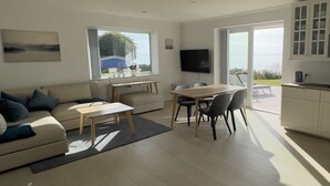 Un soggiorno moderno con un divano, un tavolo da pranzo e sedie. C'è una TV montata a parete e una finestra che offre vista sull'esterno.