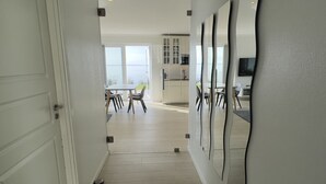 Un interno moderno con pavimento in legno, una zona pranzo con sedie e tavolo, e una cucina con mobili e piano di lavoro.