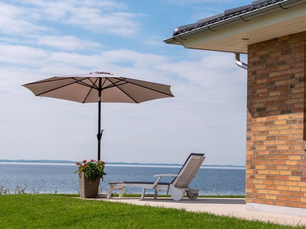 Une terrasse avec un fauteuil de relaxation et un parasol, donnant sur une étendue d’eau.