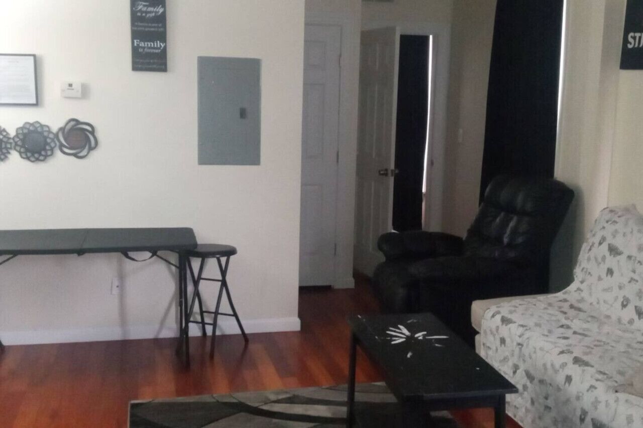A living room with a sofa, a chair, a small table, and a bench. There is a door leading to another room.
