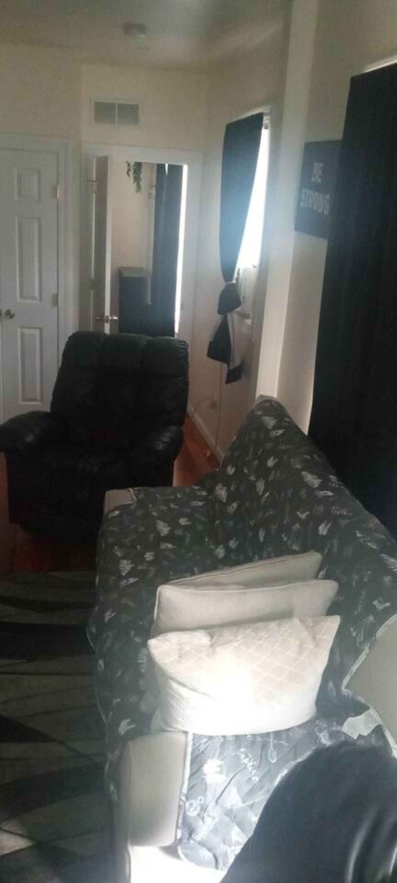 A living room with a patterned sofa, a black leather chair, and a door leading to another room.