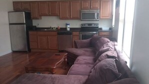 A spacious living room with a large sectional sofa, a wooden coffee table, and a kitchen area with wooden cabinets and appliances. - 1 bedroom with free parking (Schenectady)