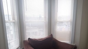 A room with a brown sofa and ottoman, white blinds on the windows, and wooden flooring. - 1 bedroom with free parking (Schenectady)