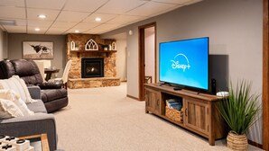 A living room with a fireplace, a leather couch, a flat-screen TV, and a wooden entertainment center. - Hot Tub | Built in Fire Pit | Fenced Yard for Kids (Fargo)