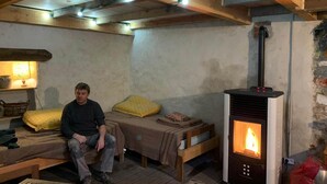 A rustic room with a bed, a small table, and a wood-burning stove.