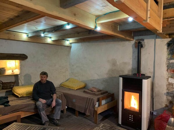 Ein rustikales Zimmer mit einem Bett, einem kleinen Tisch und einem Kaminofen.