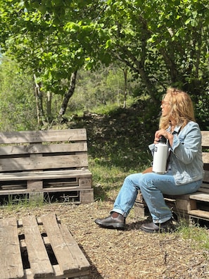 Une personne est assise sur un banc en bois Ă lâextĂ©rieur et tient un objet blanc dans sa main.