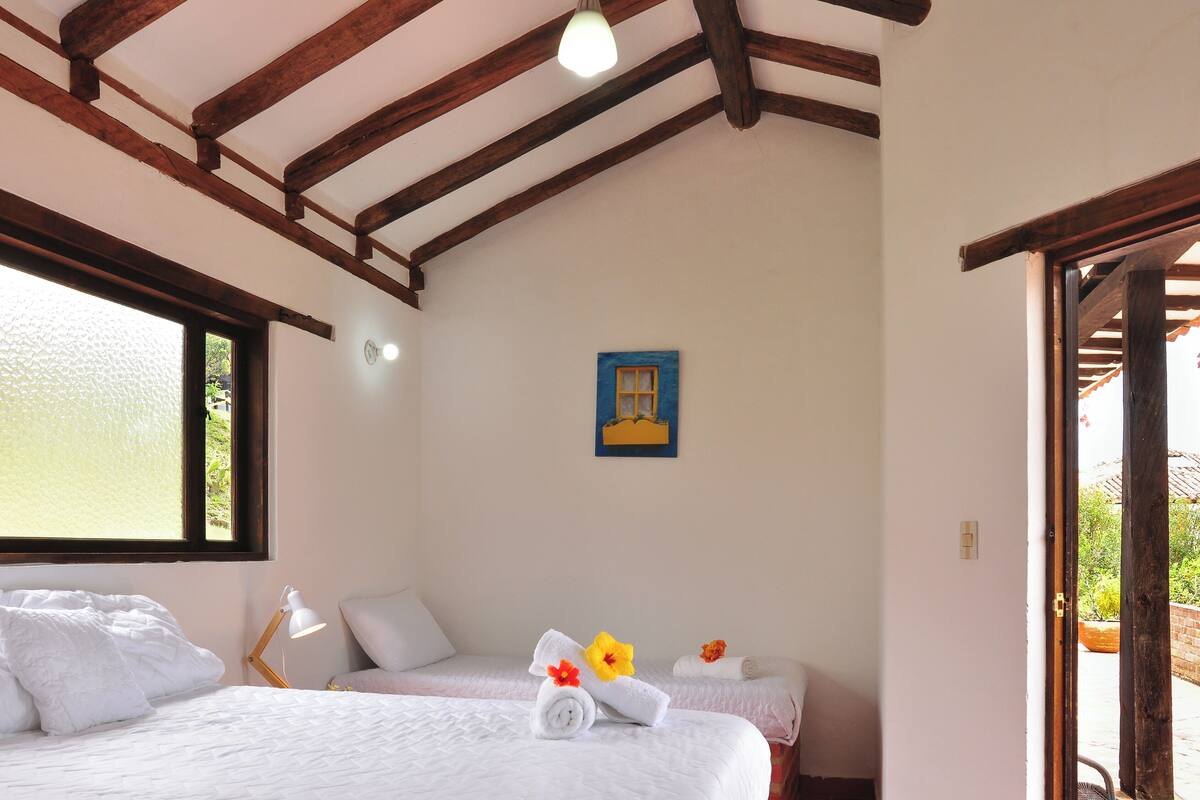 Une chambre avec deux lits, des poutres en bois au plafond, une fenêtre et une porte donnant sur l’extérieur.