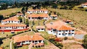 Zona residencial con casas de paredes blancas y tejados de tejas rojas, rodeada de vegetación y un paisaje montañoso.