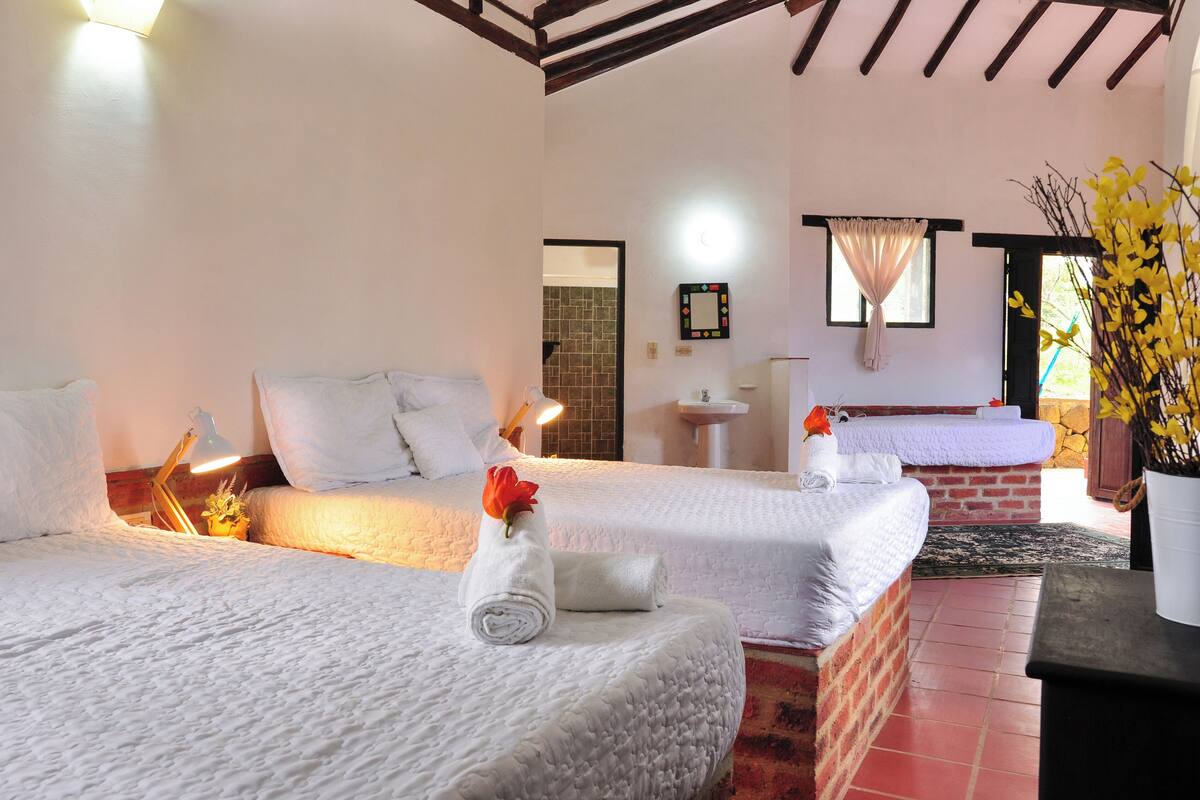 Une chambre d’hôtel avec deux lits, une petite table, une table de chevet, une lampe, un miroir et une fenêtre avec des rideaux.